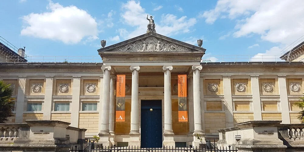 Das Bild zeigt den Eingang vom Ashmolean Museums der Universität Oxford. Es sieht aus wie ein griechischer Tempel mit 4 Säulen und einer Staue auf der Spitze des Dachs. 